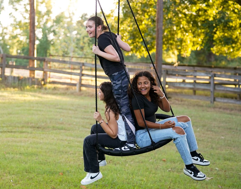 Three teen girls swinging on a tree swing